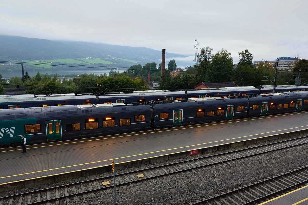 Utsikten fra hotellrommet mitt i Lillehammer, rett ned på togsporene der det står et tog og venter på avgang. Ute er det grått og vått og tåkete, og fjellene i horisonten er innhyllet i et slør av dis